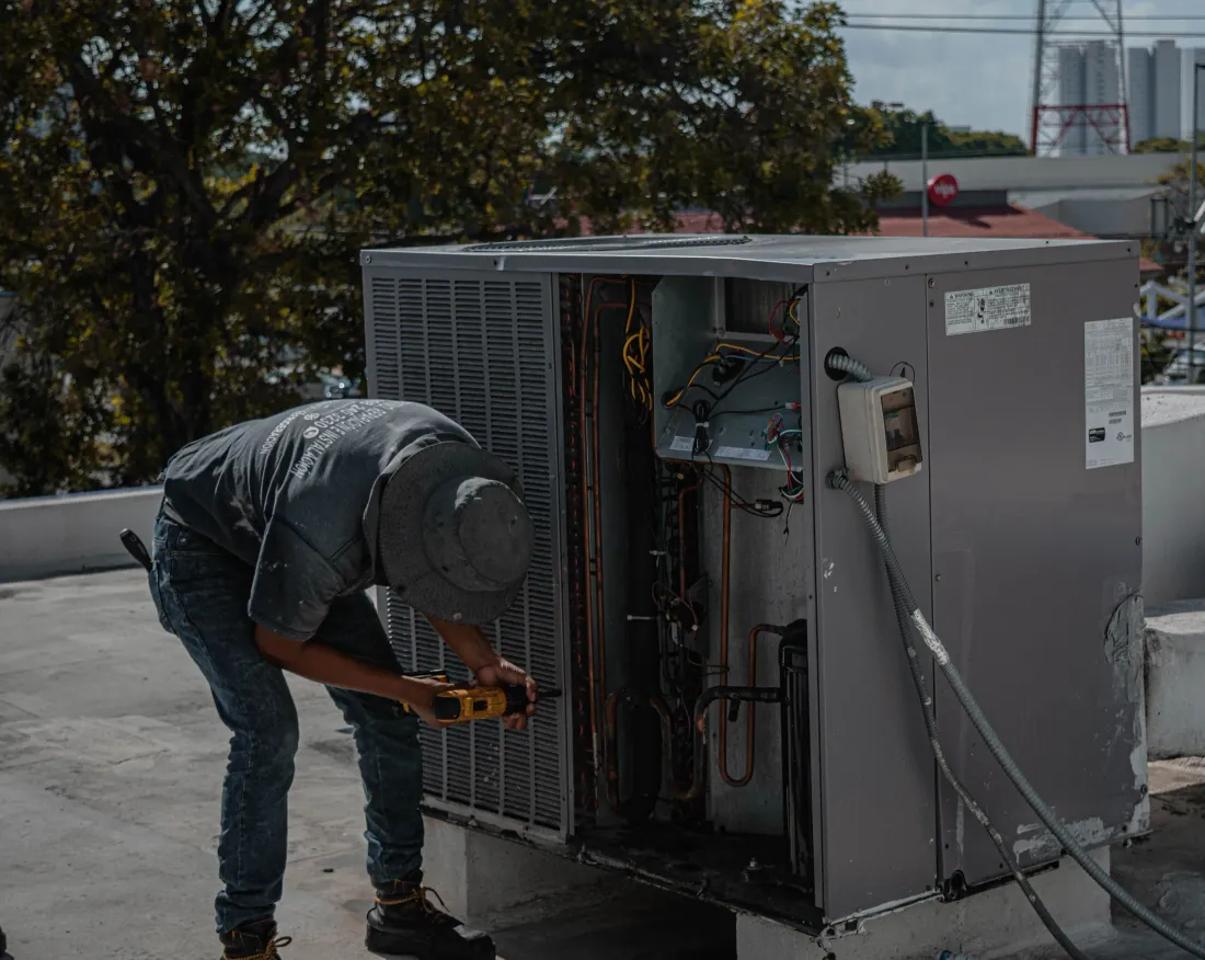 An HVAC technician repairing an outdoor air conditioning condenser unit